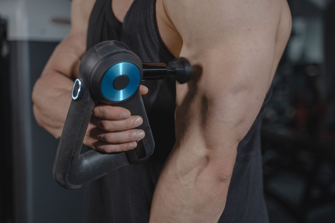Close-up of a person using a massage gun on their arm for muscle recovery