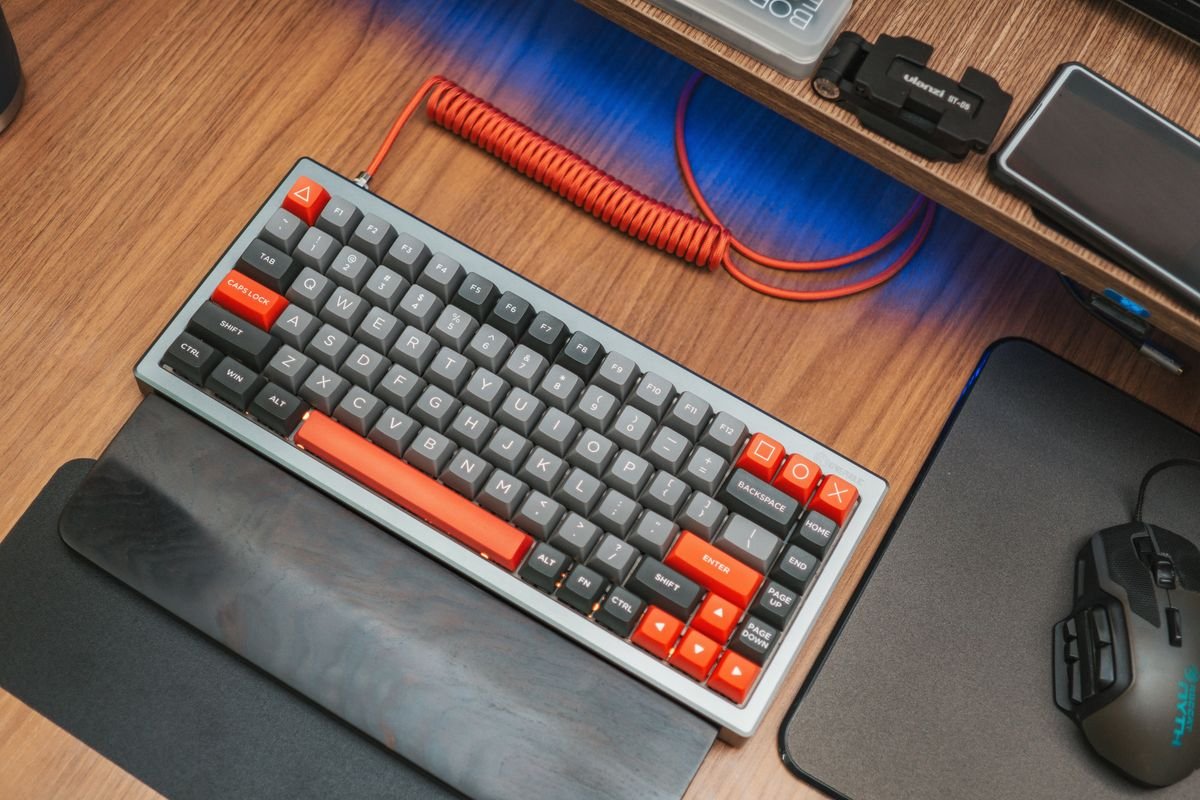 Compact mechanical keyboard with red accent keycaps on a wooden desk